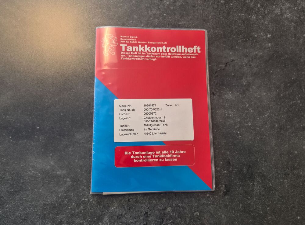 Rot-blaues Tankkontrollheft auf Betonboden – wichtiges Dokument für Heizöltank-Besitzer im Kanton Zürich