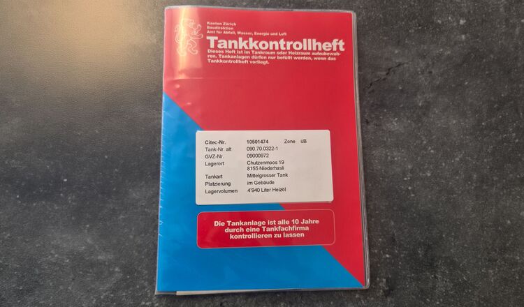 Rot-blaues Tankkontrollheft auf Betonboden – wichtiges Dokument für Heizöltank-Besitzer im Kanton Zürich